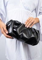 Person holding a black leather clutch against a white background
