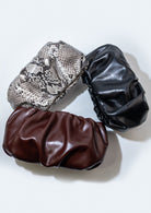 Three leather clutches in snake print, Bordeaux, and black on a white background